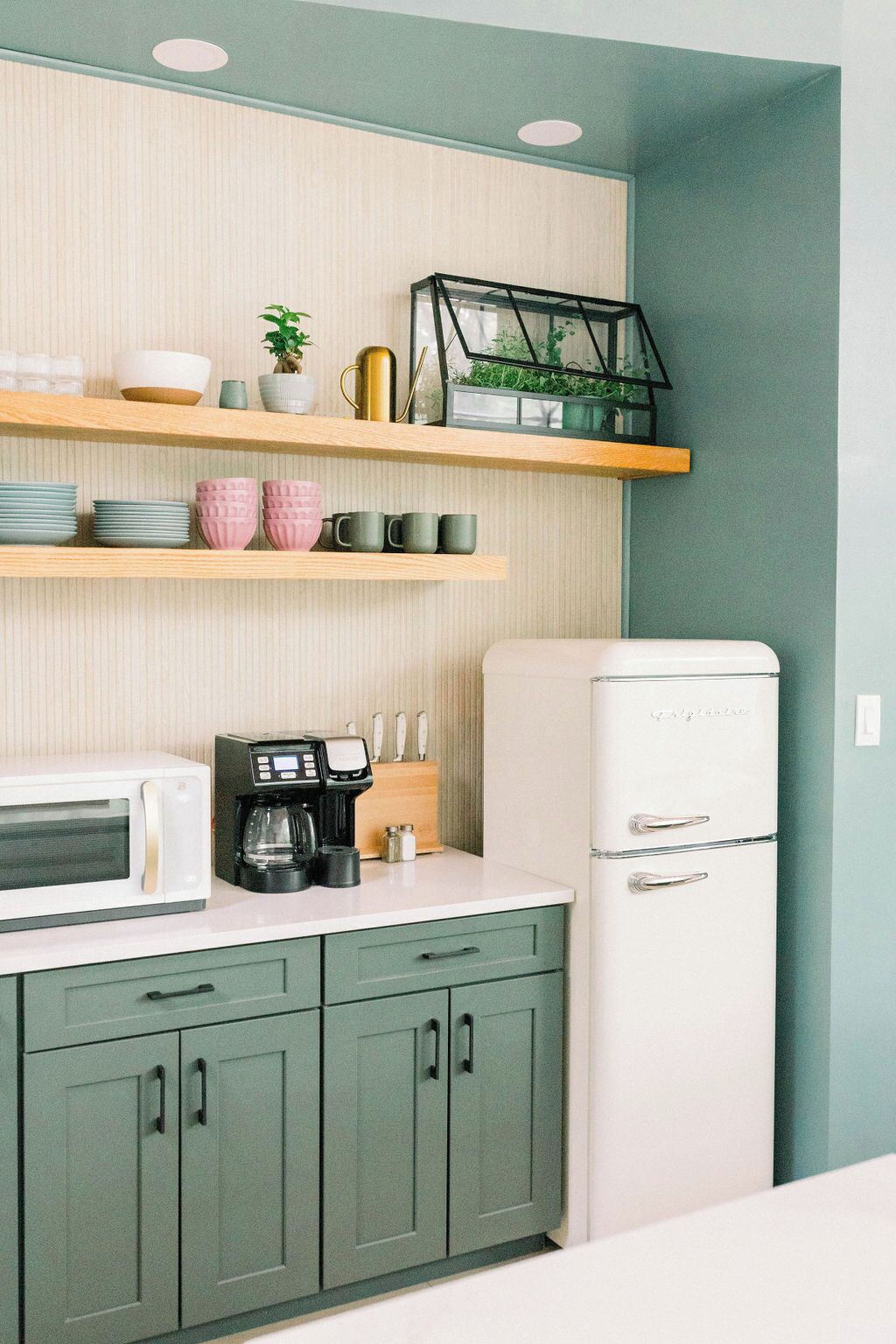 Una cocina con refrigerador blanco, microondas, cafetera y alacenas verdes.
