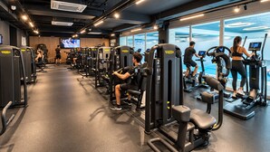A gym with various exercise machines, a cardio area, and a TV screen displaying a workout video. - Arbed Living Hotel (Arbedo-Castione)