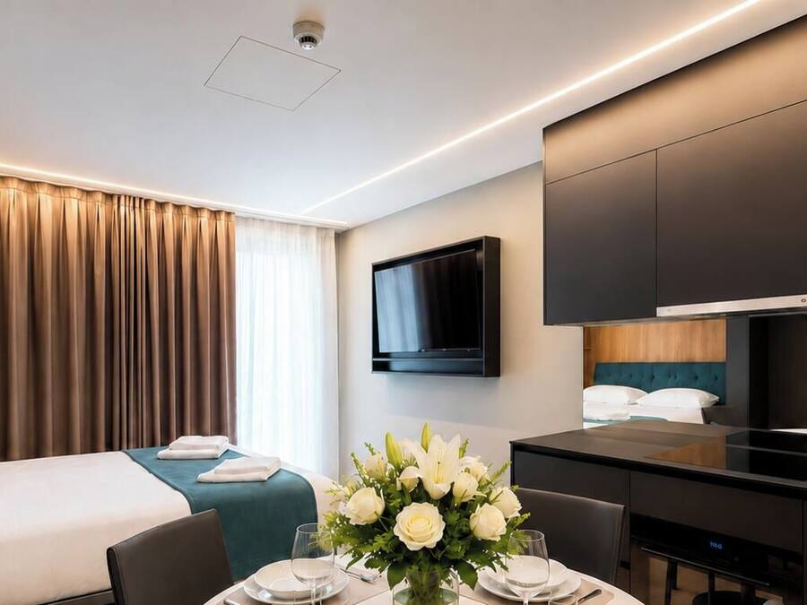 Quarto de hotel com cama, escrivaninha, televisão de tela plana e área de refeições com um vaso de flores.