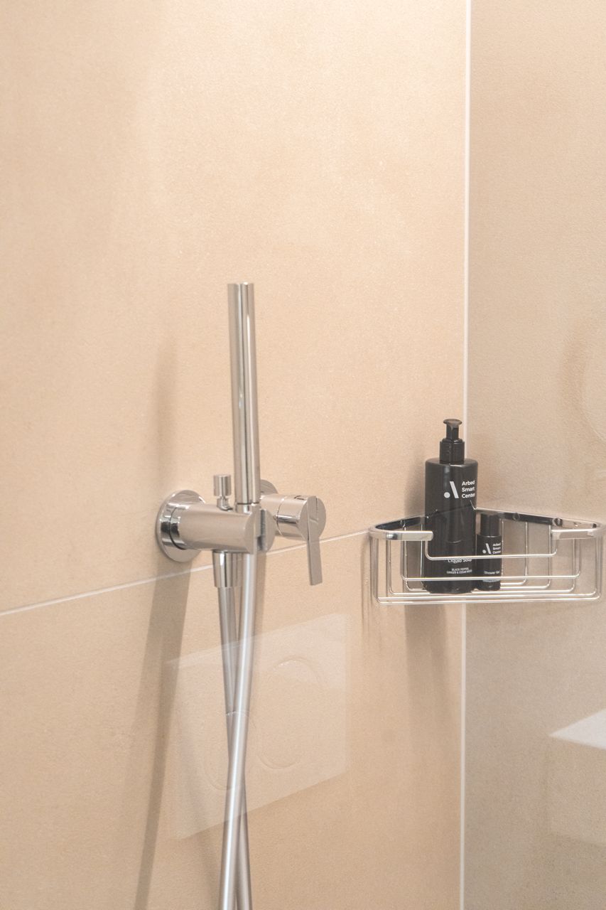 A bathroom with a chrome showerhead and a soap dispenser in a clear plastic holder.