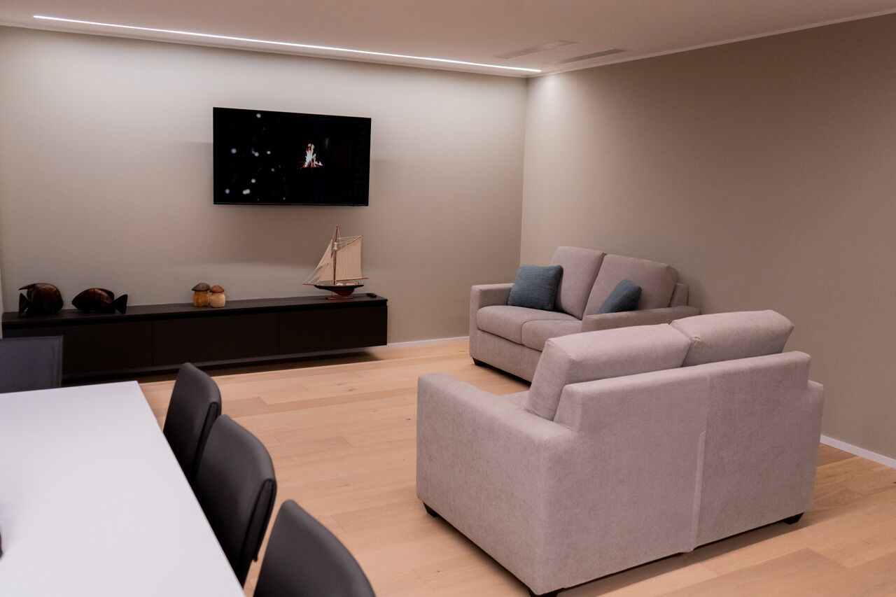 Un salon moderne avec un téléviseur à écran plat fixé au mur, un canapé et une table à manger avec des chaises.