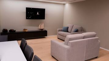 Una sala de estar moderna con un televisor de pantalla plana montado en la pared, un sofá y una mesa de comedor con sillas.