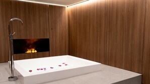Ein modernes Badezimmer mit einer weißen Badewanne, Holzpaneelen und einem eingebauten Kamin.