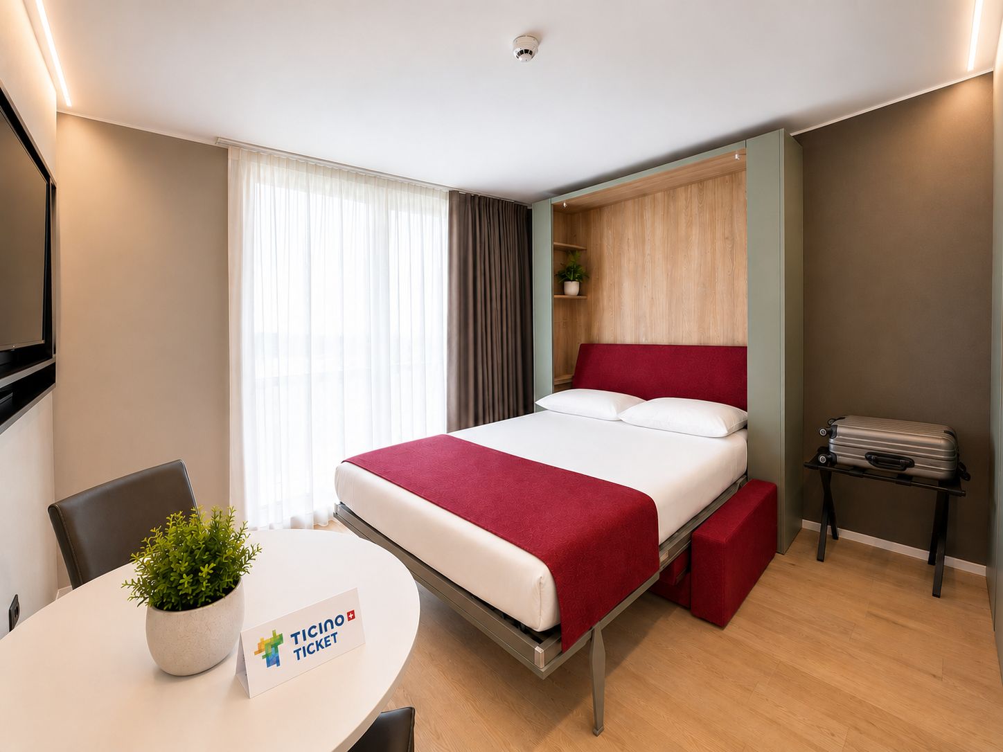 Une chambre d’hôtel avec un lit, une petite table sur laquelle est posée une plante, un banc rouge, un porte-bagages et une étagère murale agrémentée d’une plante.