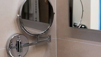 A bathroom with a round mirror mounted on the wall, a black bottle of liquid soap, and a black electrical outlet.