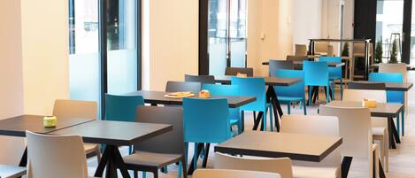 A modern dining area with multiple tables and chairs, large windows, and a clean, contemporary design.