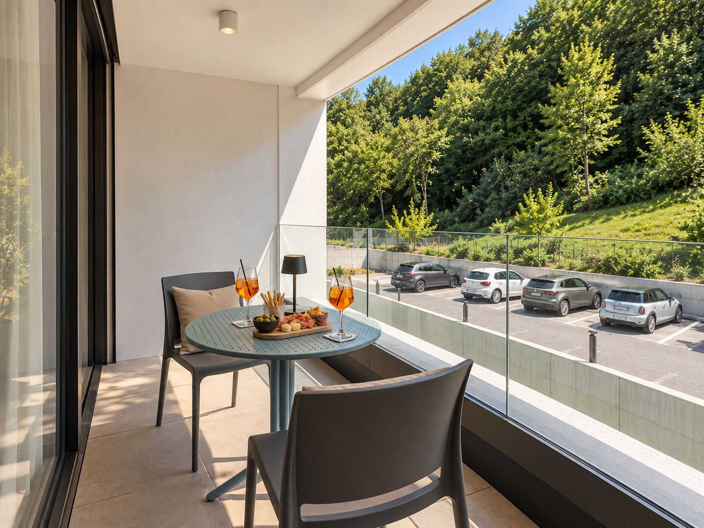 Ein Balkon mit Tisch für zwei Personen, mit Blick auf einen Parkplatz und eine grüne Landschaft.