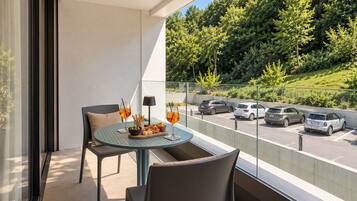 Ein Balkon mit Tisch für zwei Personen, mit Blick auf einen Parkplatz und eine grüne Landschaft.