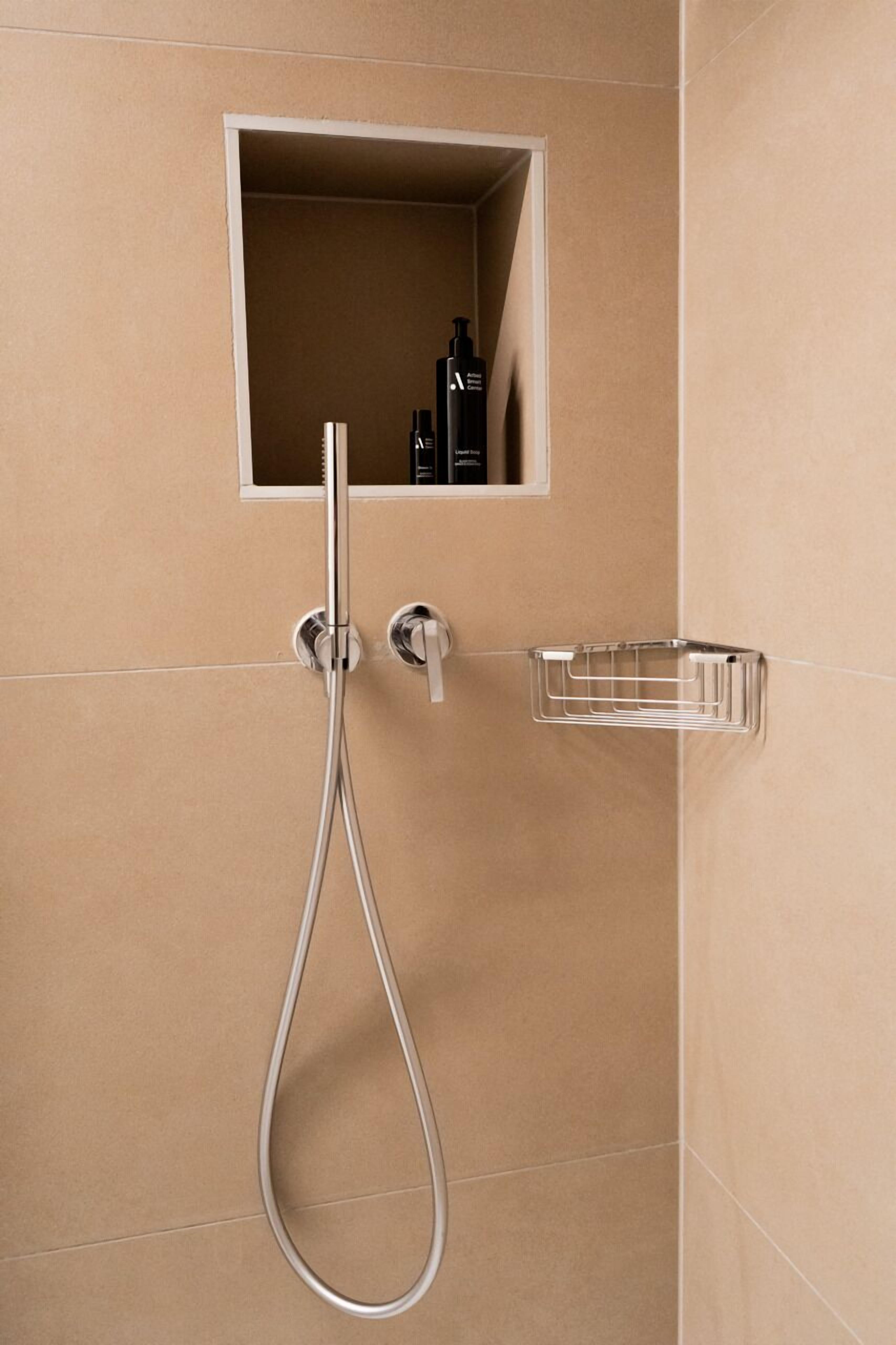 Un angolo doccia con rubinetteria cromata, soffione a mano e un piccolo ripiano con articoli da toilette.