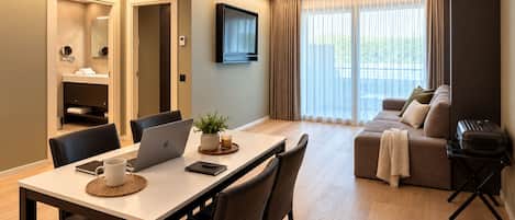 A modern hotel room with a dining area, a sofa, and a television.
