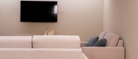 A modern living room with a large flat-screen TV mounted on the wall, a beige sofa, and a smaller armchair.