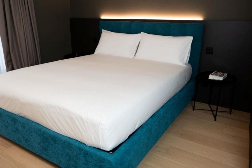 A bed with white bedding, a teal headboard, and a small bedside table with a phone and a magazine.