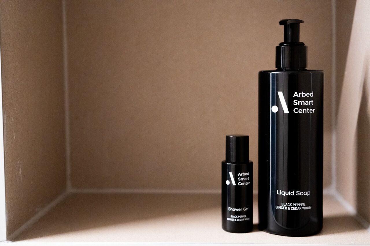 Two black bottles of Arbed Smart Center liquid soap, one labeled 'Shower Gel' and the other 'Liquid Soap' with 'Black Pepper, Ginger & Cedar Wood' scent.