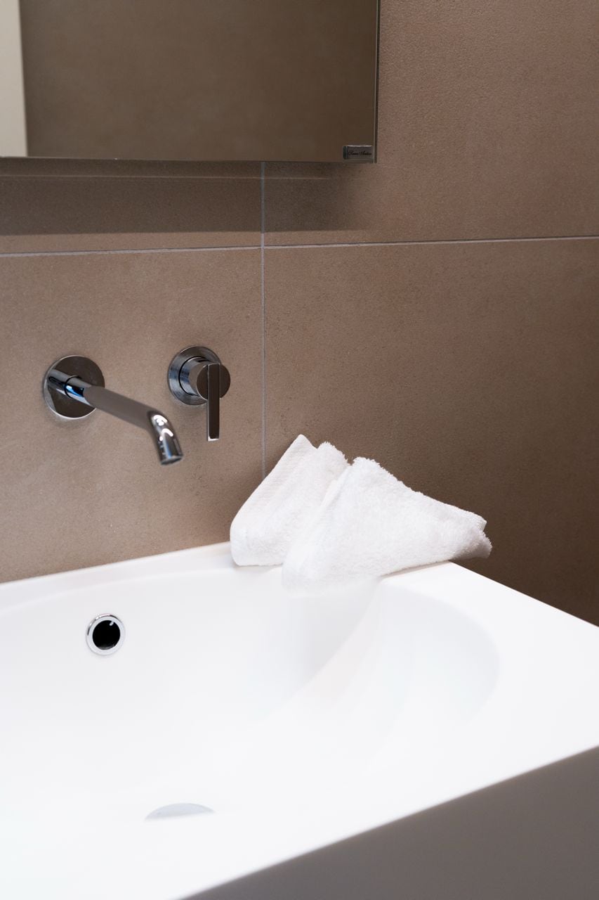 A modern bathroom with a white sink, chrome faucet, and towel hanging on a wall-mounted towel rack.