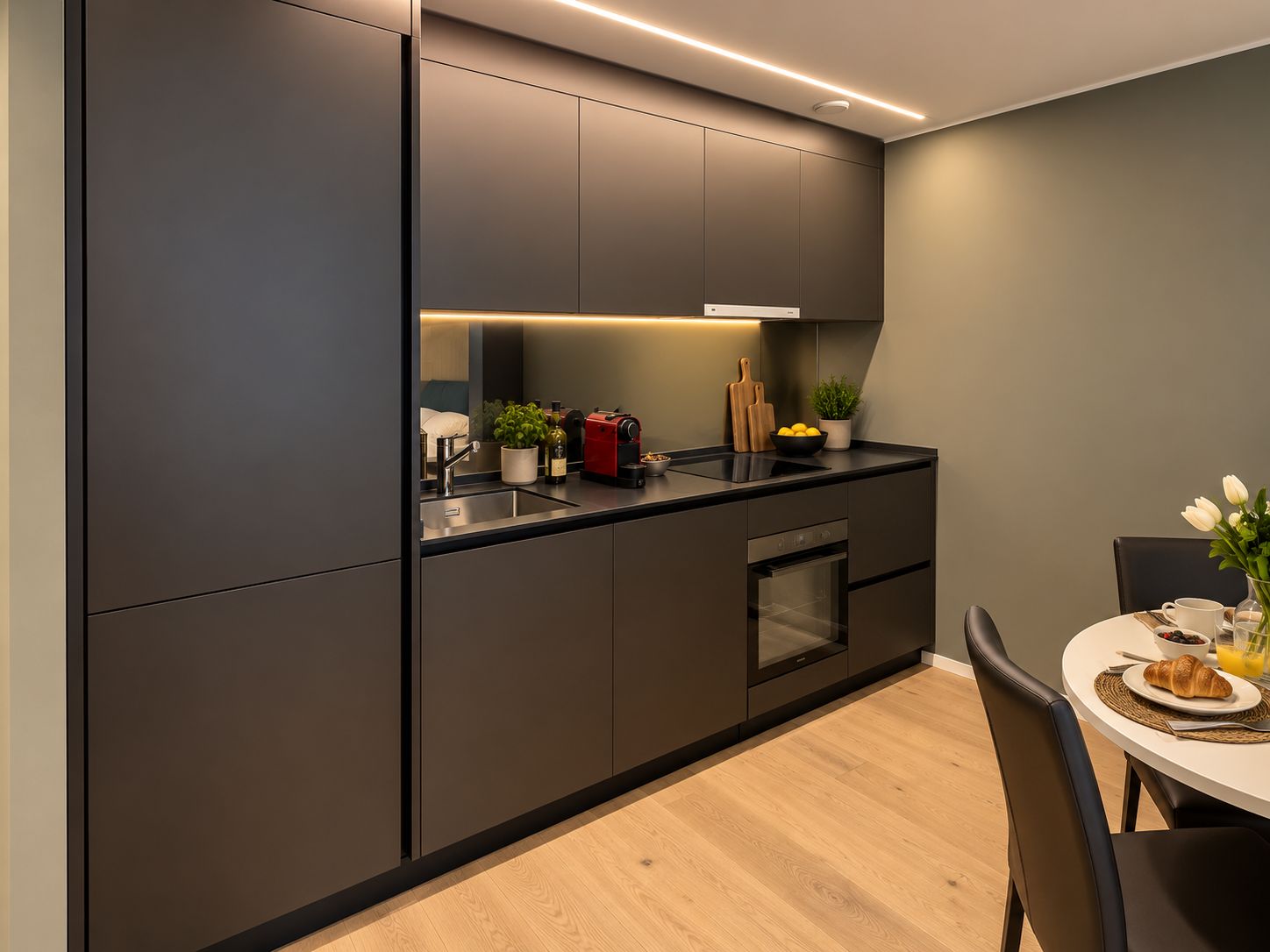 Une cuisine moderne équipée d’un four encastré, d’un évier et d’un coin repas avec une table et des chaises.