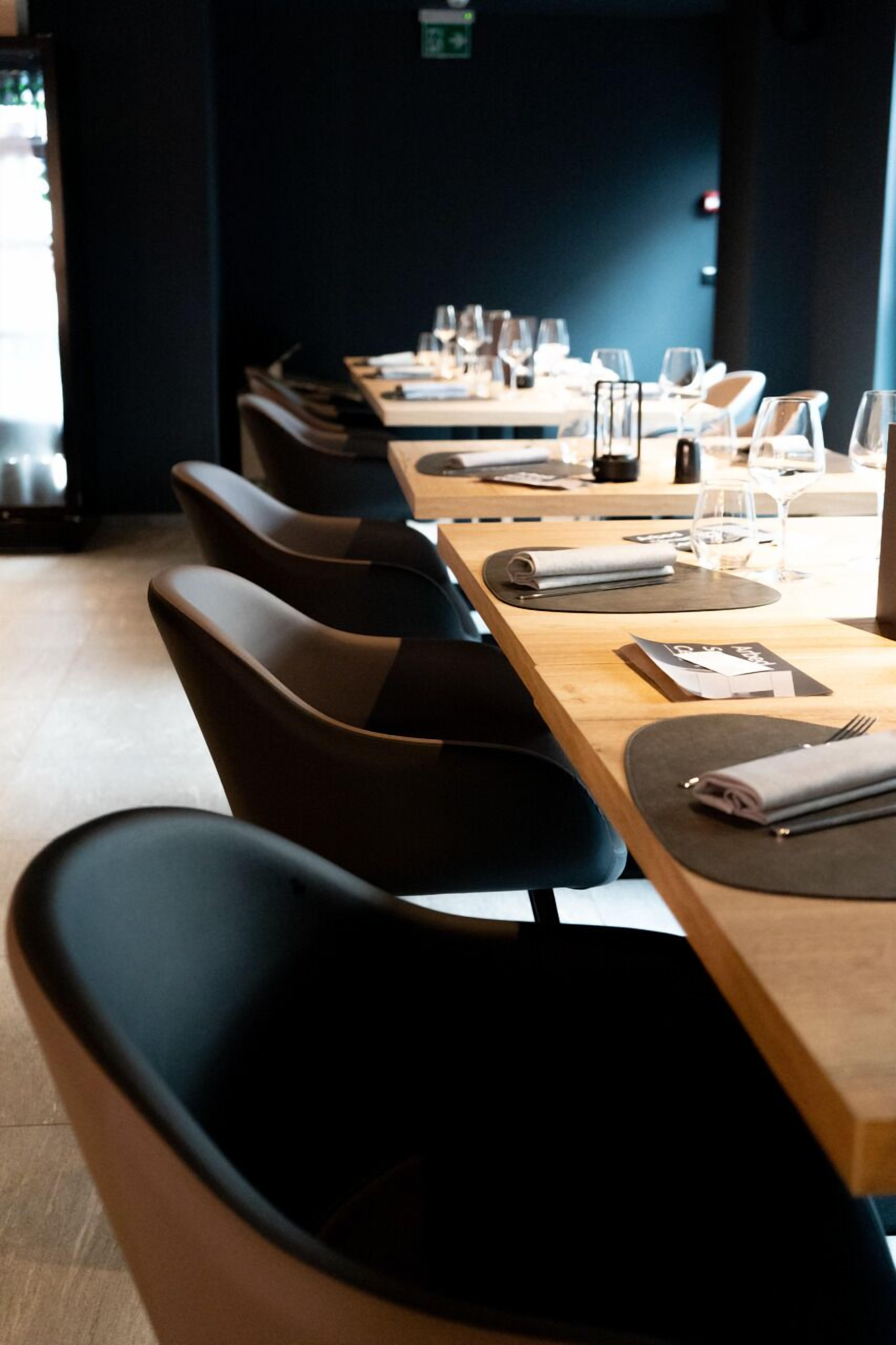 A restaurant with a long table set for dining, black upholstered chairs, and a wooden table surface.