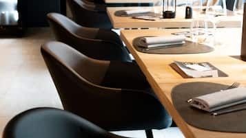 Un restaurant amb una taula llarga preparada per dinar, caires negres amb tapisseria i superfície de taula de fusta.
