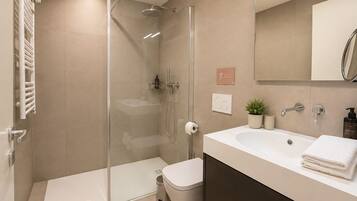 Ein modernes Badezimmer mit einer in Glas eingefassten Dusche, einem weißen Waschbecken und einer Toilette.