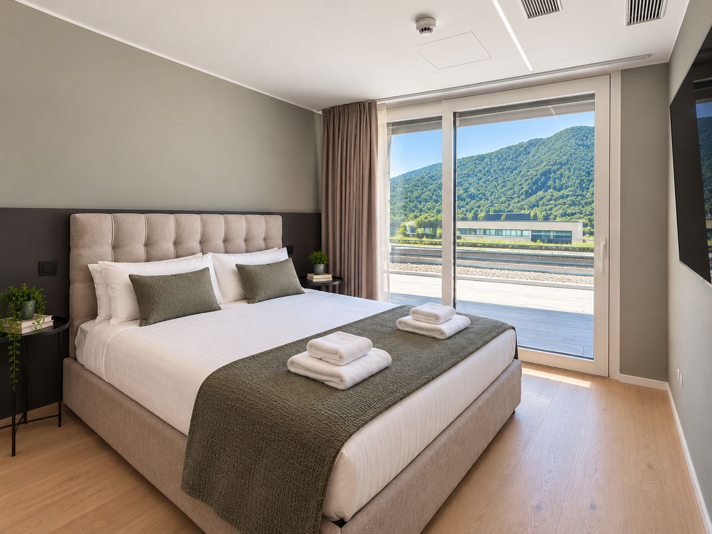 Ein modernes Hotelzimmer mit einem großen Bett, Blick auf einen Bahnhof und einem Balkon.
