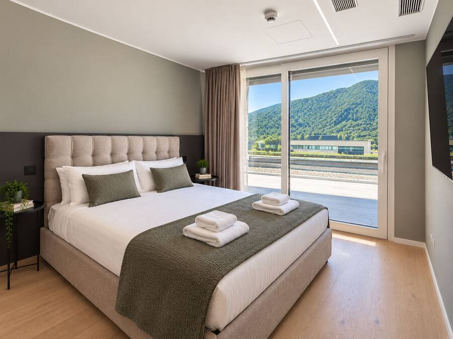 Ein modernes Hotelzimmer mit einem großen Bett, Blick auf einen Bahnhof und einem Balkon.