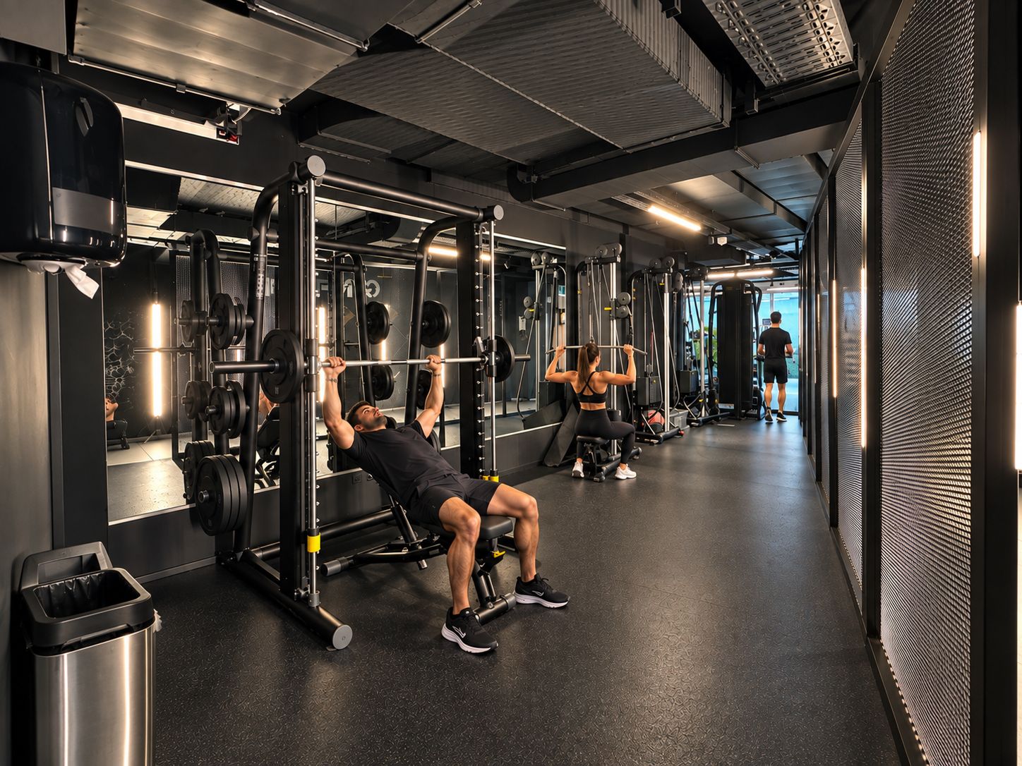 Ein Fitnessstudio mit Gewichthebern, einem Mülleimer und einer trainierenden Person.