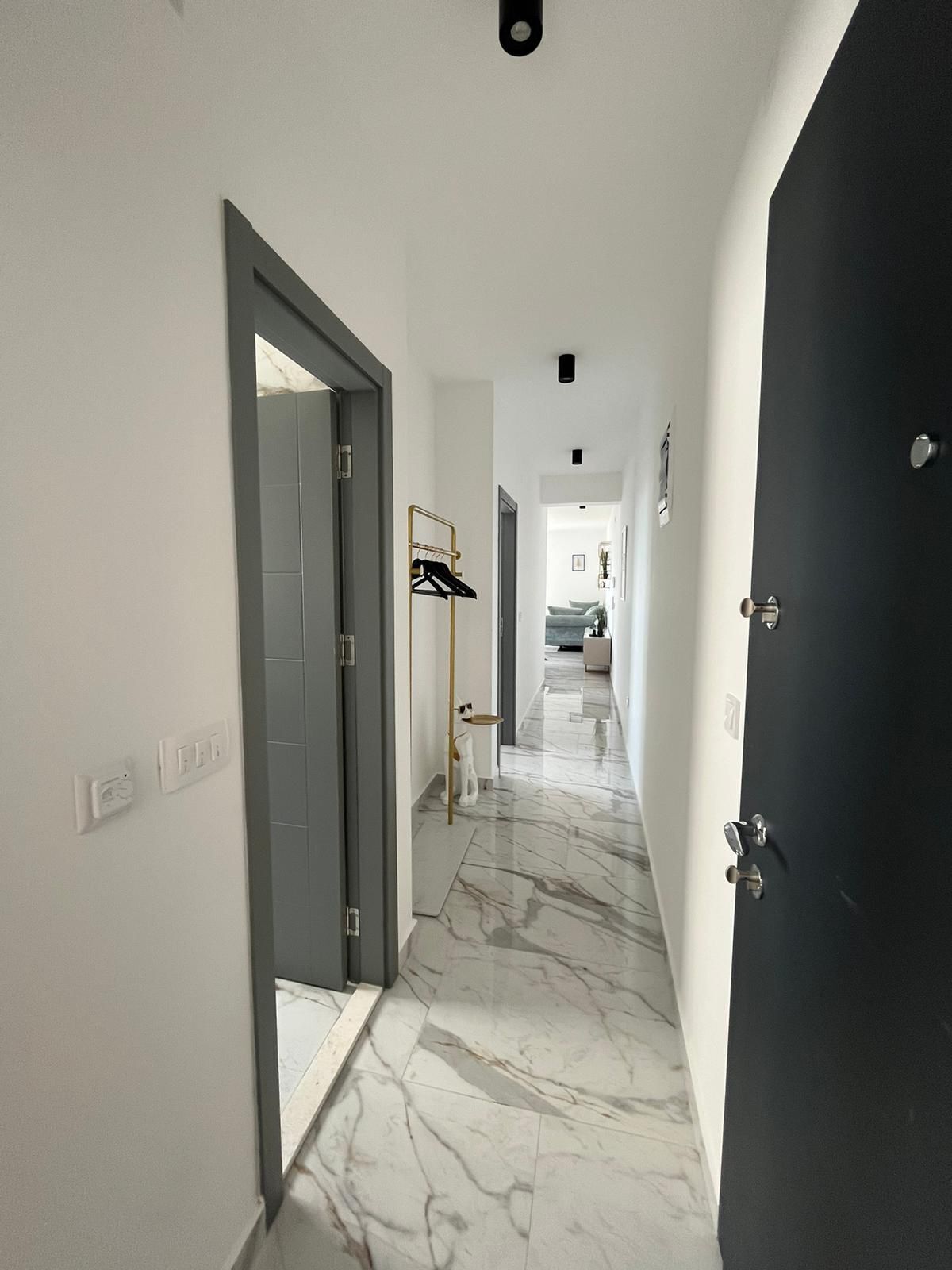 A hallway with a marble floor, a black door, and a clothing rack.