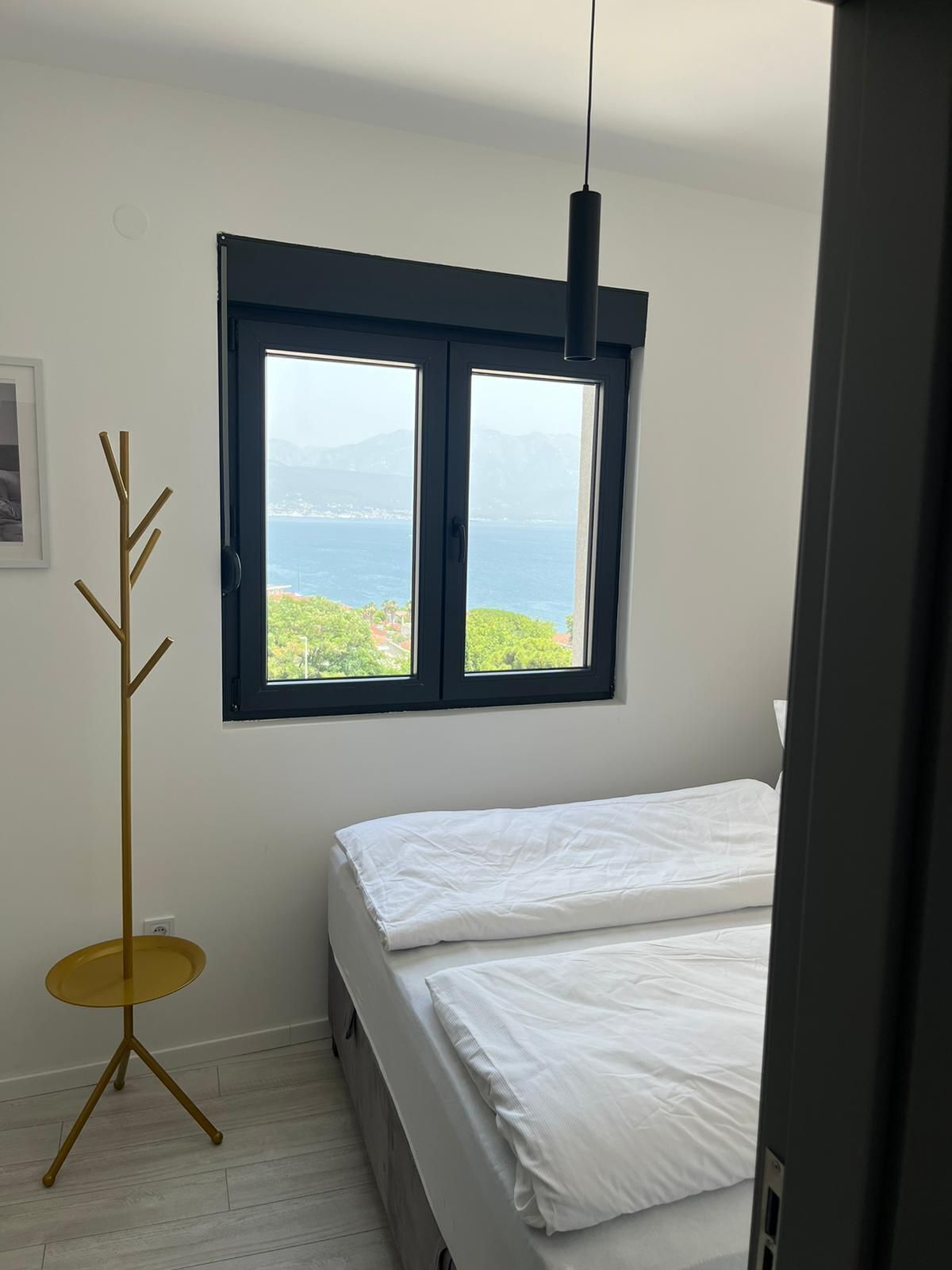 Ein Schlafzimmer mit einem Bett, einem Fenster mit Meerblick, einem Kleiderständer und einer Stehlampe.