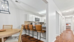 Une cuisine moderne avec des meubles blancs, un four à micro-ondes et un coin repas comprenant une table et des chaises en bois.