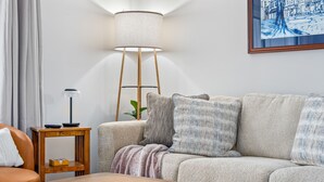 Un salon avec un canapé, une table d’appoint en bois, un lampadaire et un tableau accroché au mur.