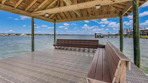 Une terrasse en bois avec un banc, un espace abrité et une vue sur l’eau et les bâtiments au loin.