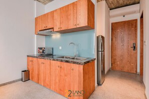 A compact kitchen with wooden cabinets, a stainless steel sink, and a built-in microwave. - 22land Residence Suite (Hanoi)