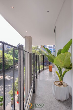 A balcony with a railing, a potted plant, and a view of a street with buildings and trees. - 22land Residence Suite (Hanoi)