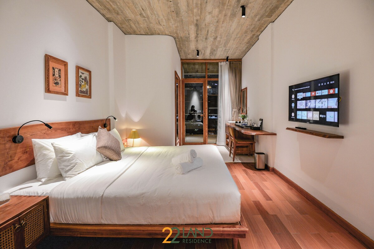 A bedroom with a wooden headboard, a bed with white linens, a television on the wall, and a wooden floor.