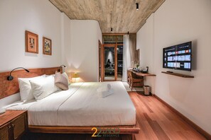 A bedroom with a wooden headboard, a bed with white linens, a television on the wall, and a wooden floor. - 22land Residence Suite (Hanoi)