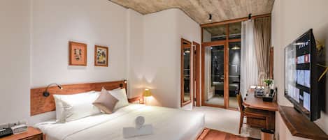 Habitación de hotel con techo de madera, cama con ropa blanca, escritorio con televisor de pantalla plana y puerta corrediza de vidrio que da a un balcón.