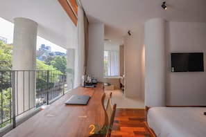A spacious room with a wooden floor, a bed, a desk with a laptop, and a TV on the wall. - 22land Residence Suite (Hanoi)