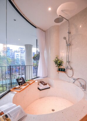 A modern bathroom with a large bathtub, a shower, and a view of the city through a large window. - 22land Residence Suite (Hanoi)
