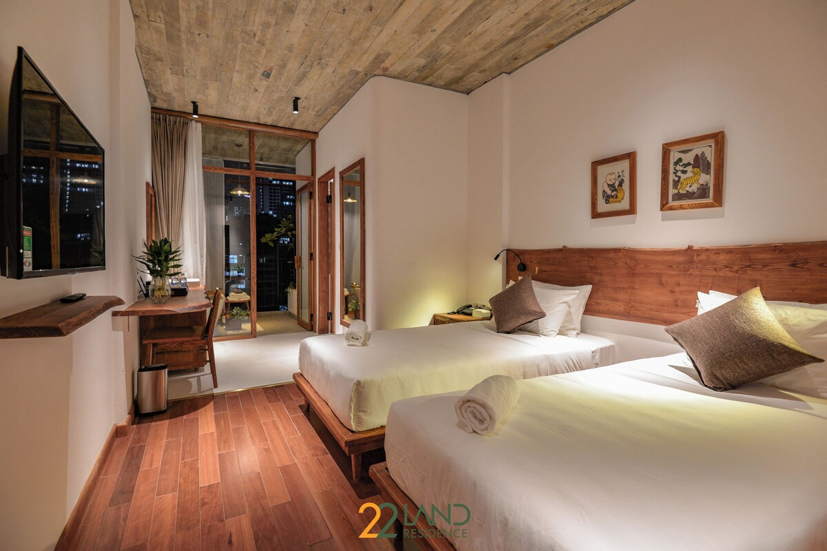 Ein Hotelzimmer mit zwei Betten, einem Holztisch, einem Stuhl, einem kleinen Tisch und einem Fenster mit Vorhängen.