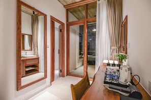 A hotel room with a wooden-framed mirror, a sink, a small plant, a tray with toiletries, and a hairdryer. - 22land Residence Suite (Hanoi)