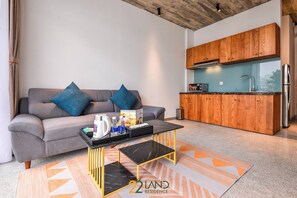 A modern living room with a grey sofa, a black coffee table, and a kitchen area with wooden cabinets and a stainless steel refrigerator. - 22land Residence Suite (Hanoi)