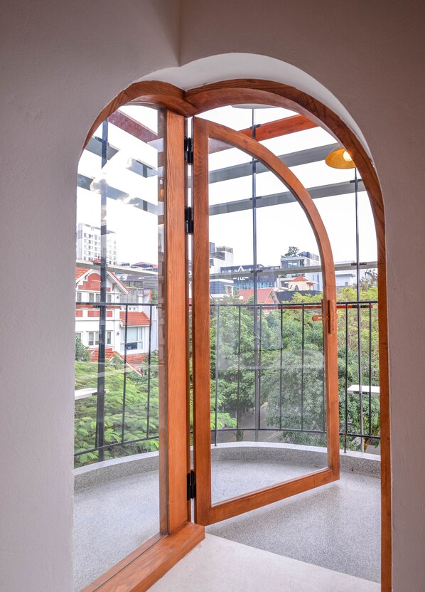 Ein Zimmer mit einem großen Bogenfenster, Blick auf Gebäude und ein Balkon mit Geländer.