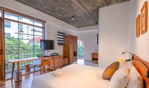 A modern hotel room with a large bed, a desk with a TV, and a balcony with a view of buildings and trees. - 22land Residence Suite (Hanoi)