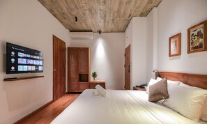 A hotel room with a bed, a TV mounted on the wall, a wooden ceiling, and a small table with a plant. - 22land Residence Suite (Hanoi)