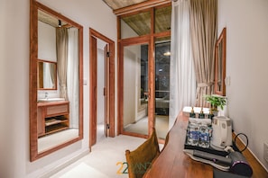 A hotel room with a wooden-framed sliding door leading to a balcony, a wooden dining table with a hairdryer and toiletries, and a small plant on the table. - 22land Residence Suite (Hanoi)
