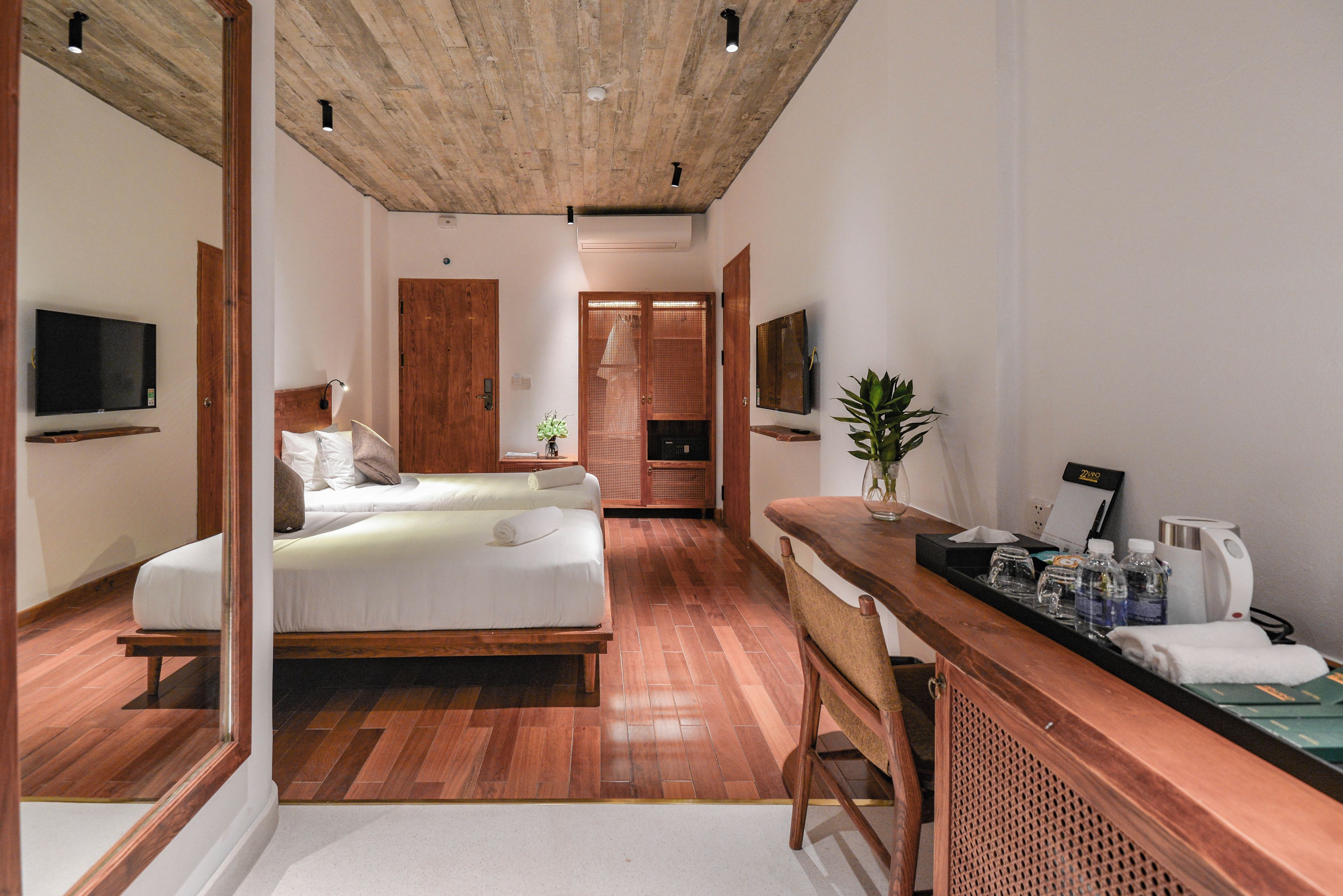 Une chambre d’hôtel moderne avec un plafond en bois, un lit, un bureau avec une chaise, une télévision et une plante.