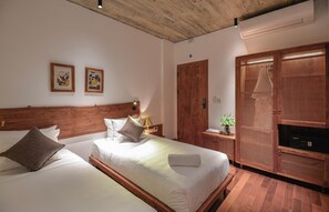 A hotel room with two beds, wooden headboards, a wooden wardrobe, and two framed pictures on the wall. - 22land Residence Suite (Hanoi)