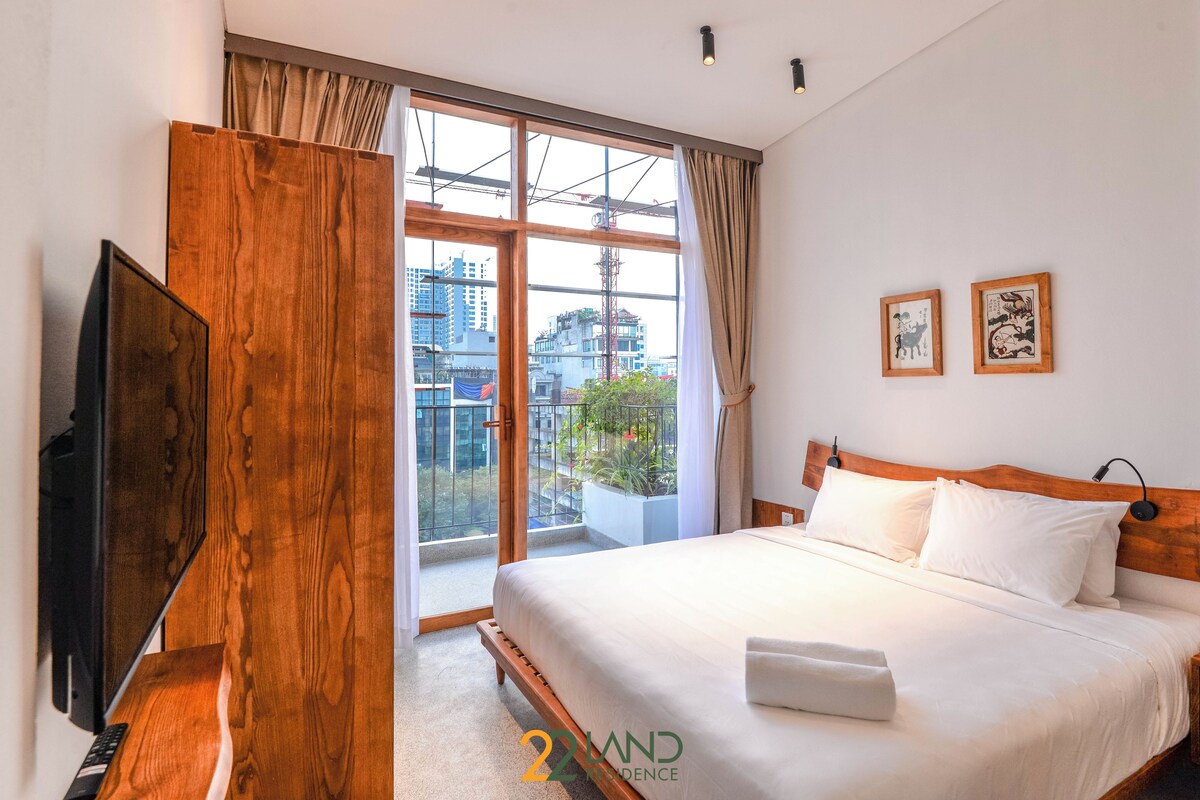Ein Hotelzimmer mit einem großen Bett, einem Fernseher und Blick auf die Stadt durch ein großes Fenster.