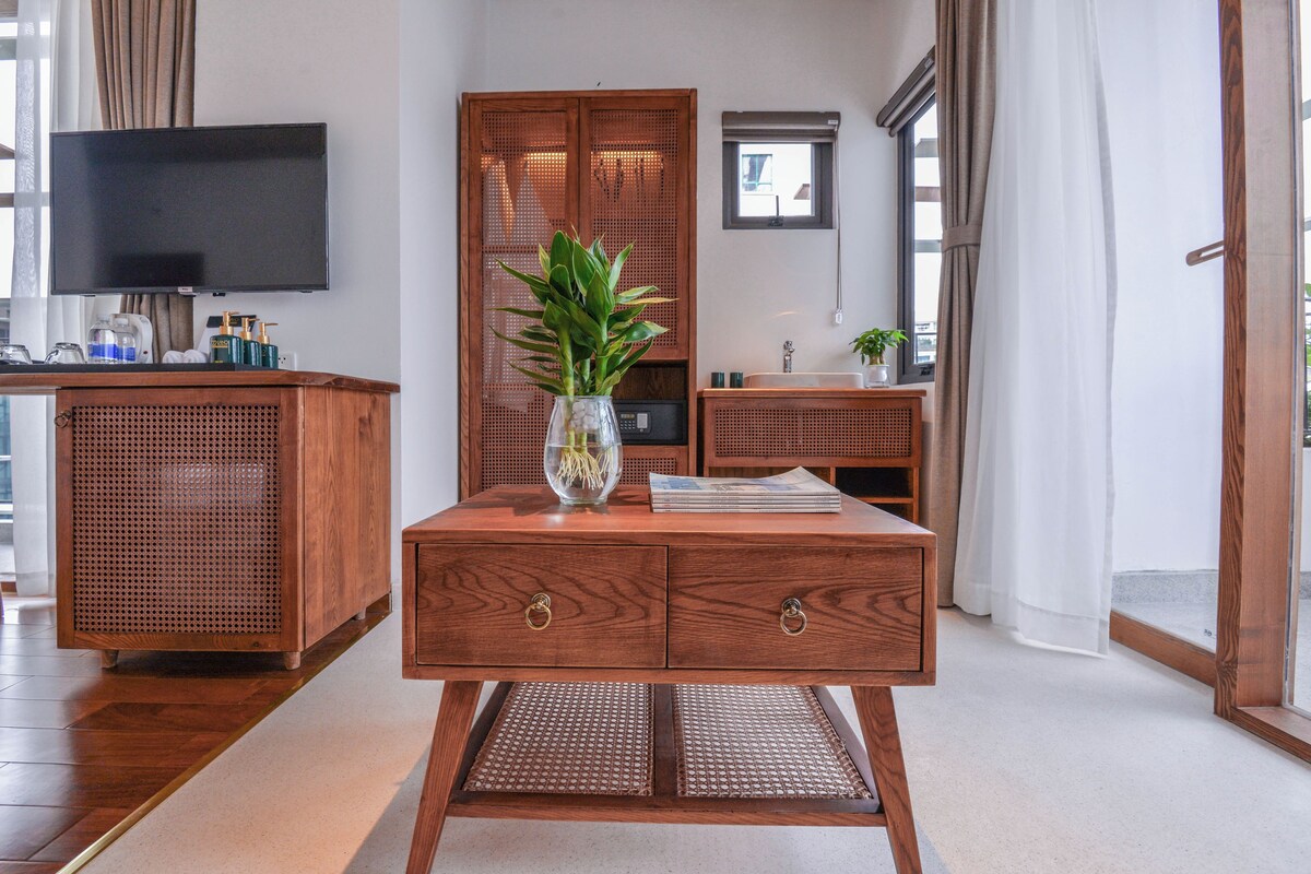 A wooden cabinet with a television above it, a plant on a table, and a window with curtains.