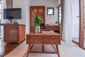 A wooden cabinet with a television above it, a plant on a table, and a window with curtains. - 22land Residence Suite (Hanoi)