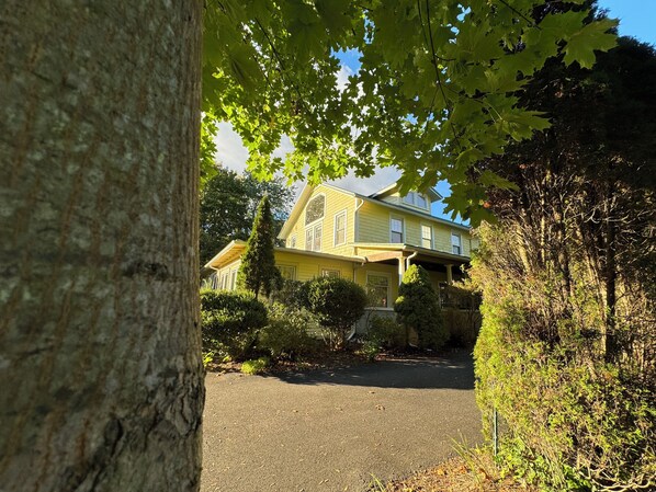 A two-story house with a front porch, surrounded by trees and shrubs.